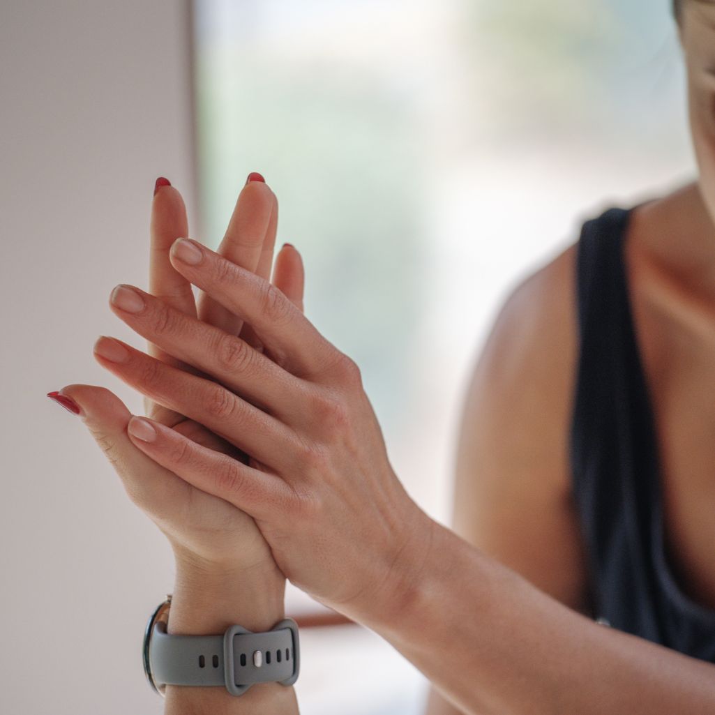 Close-up of a person's hands with red nail polish, wearing a gray watch, against a blurred background.