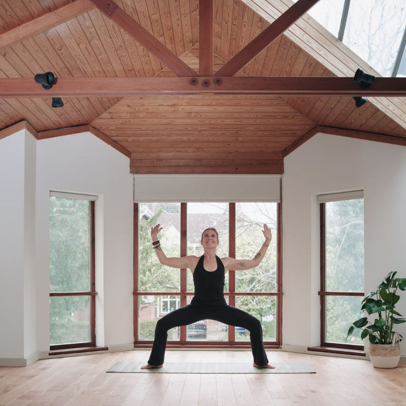 Person practicing yoga in a spacious room with large windows and wooden beams.